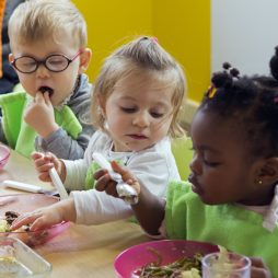 3 jeunes enfants mangent avec les doigts à table.