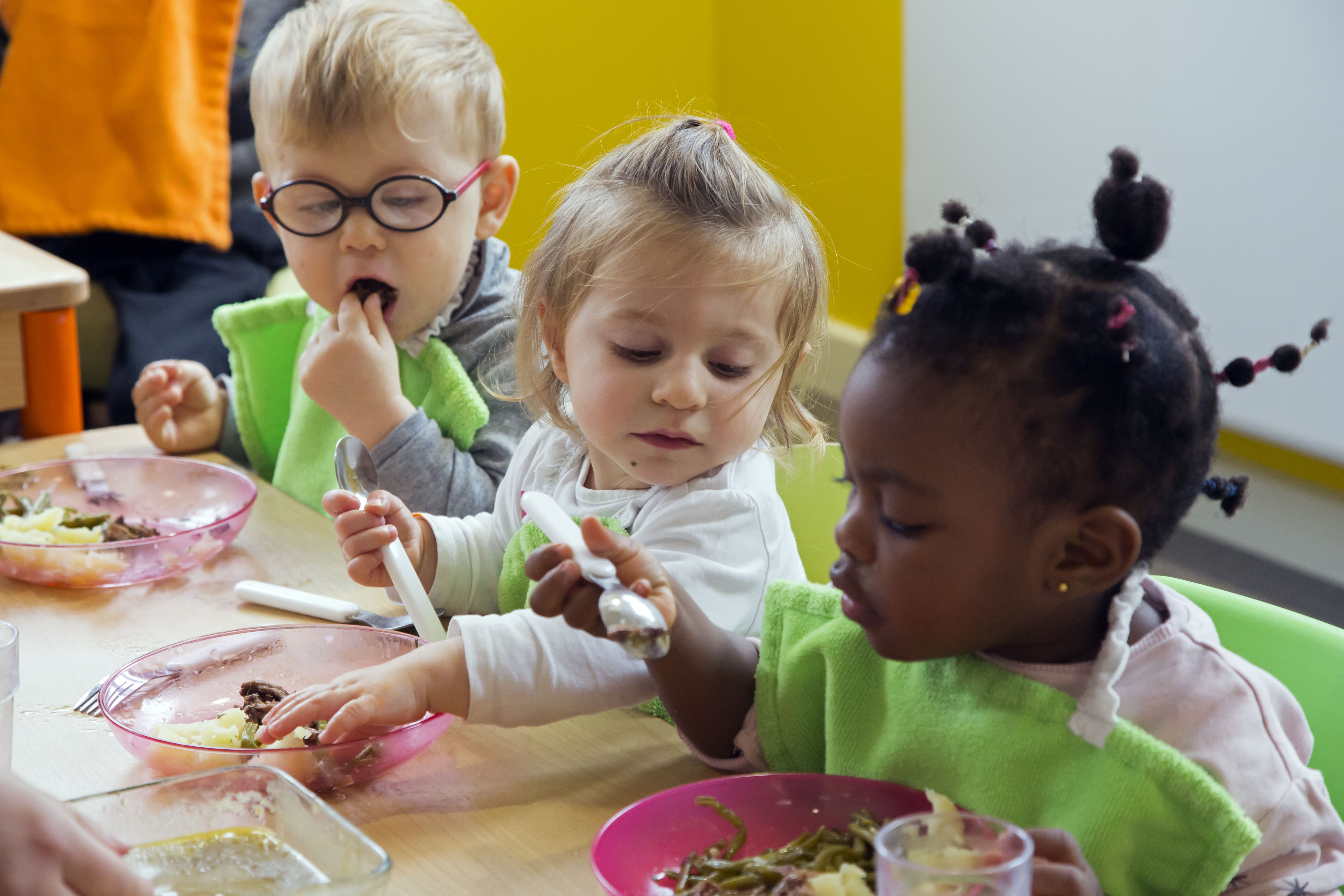 3 jeunes enfants mangent avec les doigts à table.